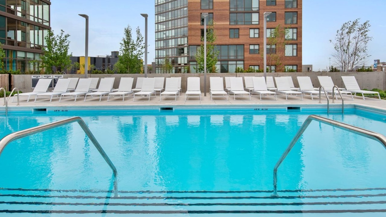 A sparkling outdoor swimming pool at Spoke Apartments in Chicago, surrounded by lounge chairs and modern buildings
