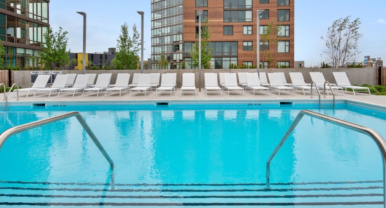 A sparkling outdoor swimming pool at Spoke Apartments in Chicago, surrounded by lounge chairs and modern buildings