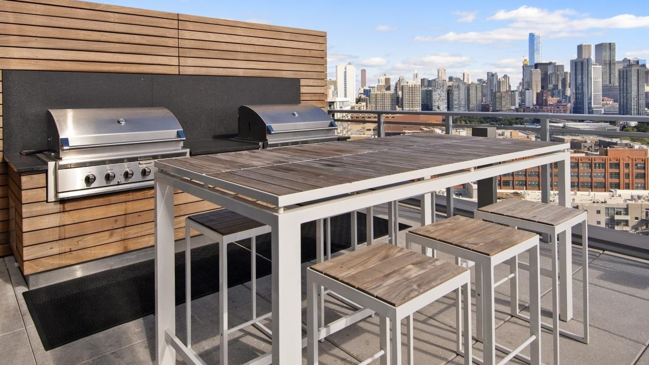 A rooftop grilling station at Spoke Apartments in Chicago, with a large dining table and stunning city views