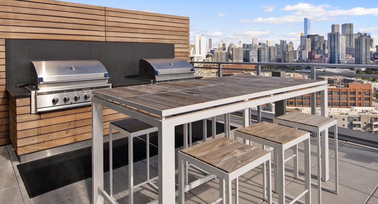 A rooftop grilling station at Spoke Apartments in Chicago, with a large dining table and stunning city views