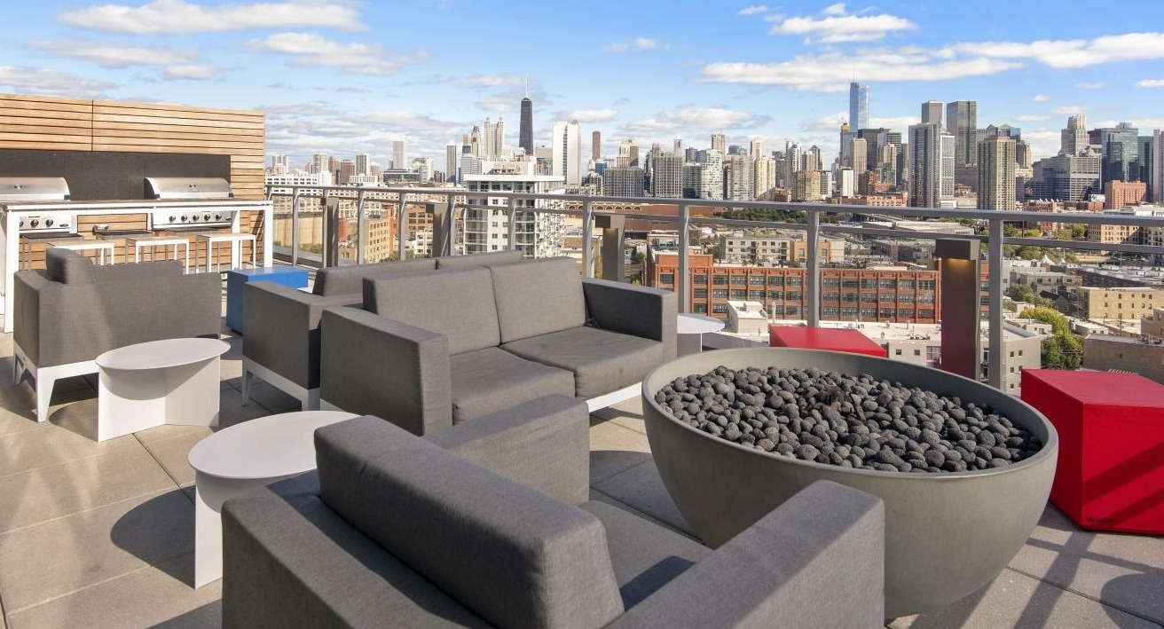 A rooftop lounge at Spoke Apartments in Chicago, complete with comfortable seating, a fire pit, and stunning city views