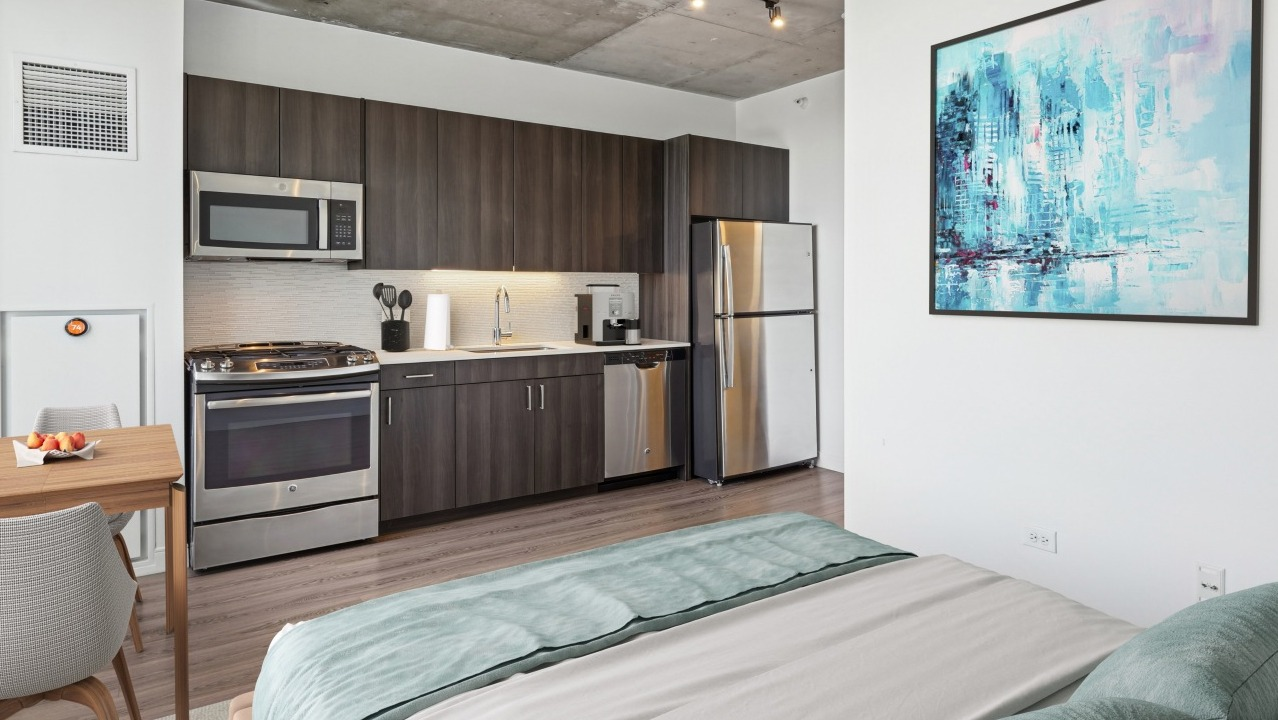 A modern studio apartment at Spoke in Chicago, showcasing a compact kitchen and a comfortable bedroom area