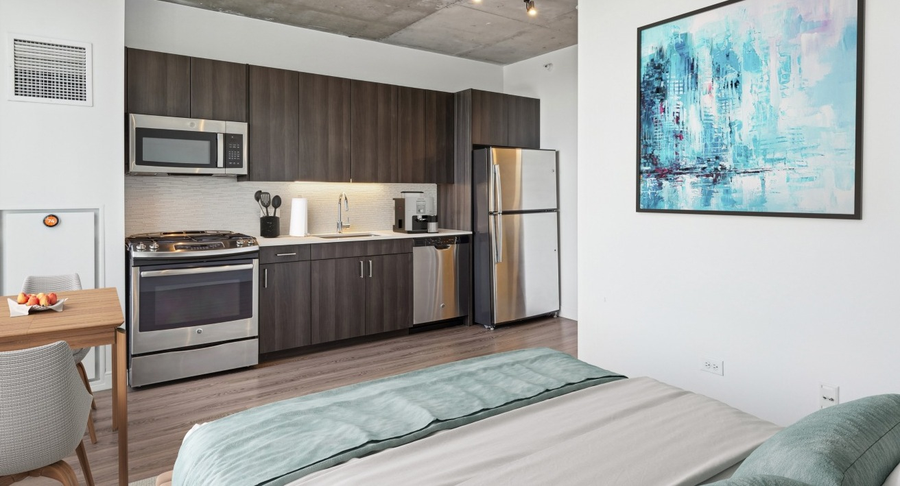 A modern studio apartment at Spoke in Chicago, showcasing a compact kitchen and a comfortable bedroom area