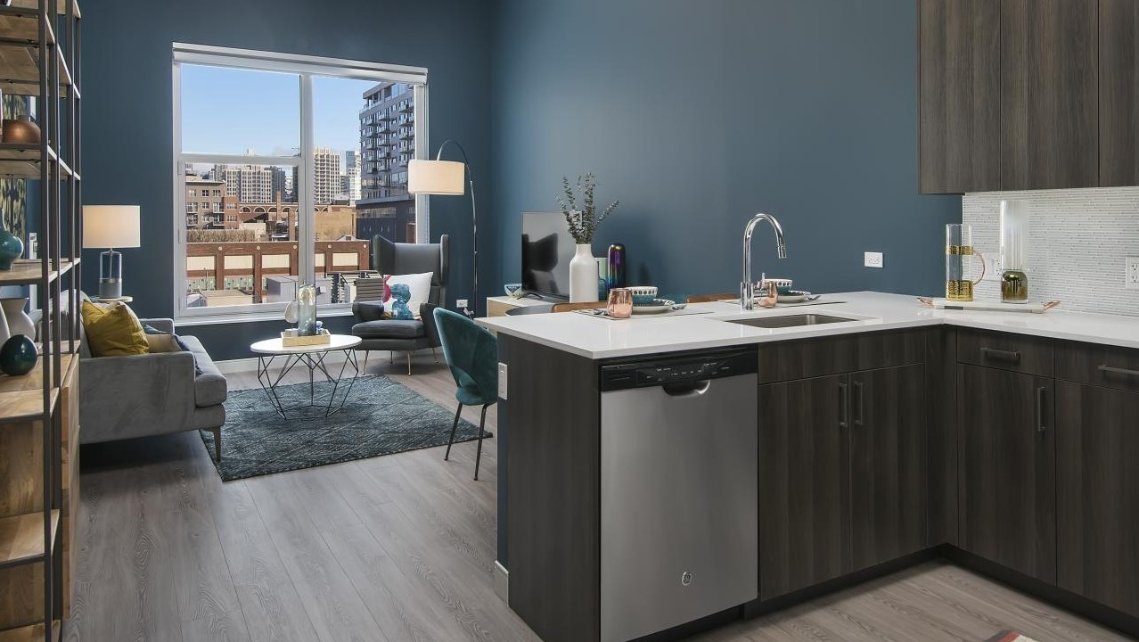 A stylish kitchen and living area at Spoke Apartments in Chicago, with dark cabinetry and a striking blue wall