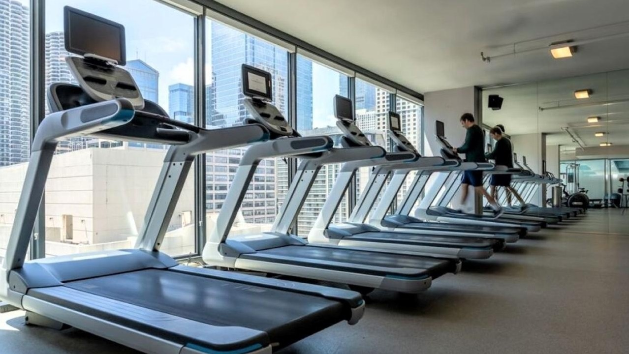 State-of-the-art fitness center with rows of treadmills and other cardio equipment facing large windows with city views at State and Grand Apartments in Chicago