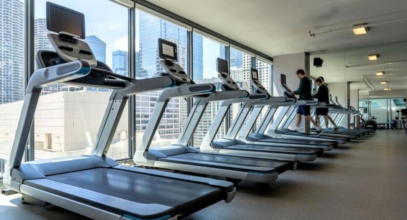 State-of-the-art fitness center with rows of treadmills and other cardio equipment facing large windows with city views at State and Grand Apartments in Chicago