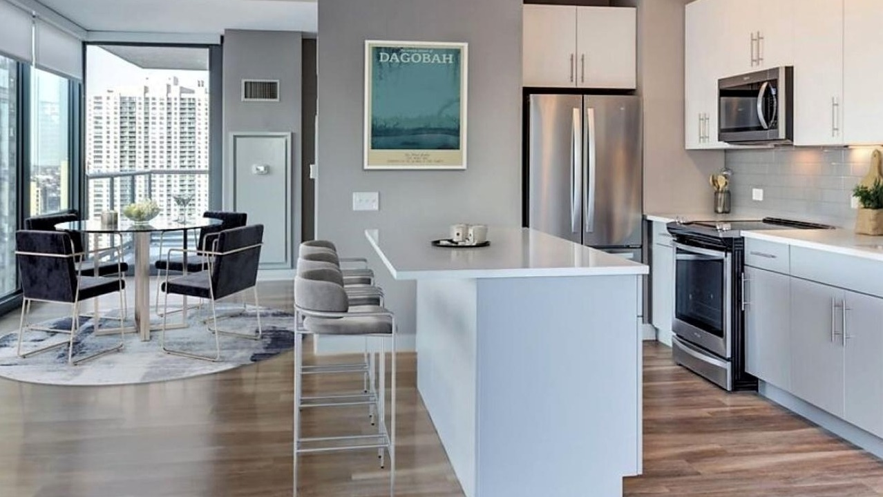 Contemporary kitchen with white cabinets, stainless steel appliances, a large island with bar seating, and an adjacent dining area at State and Grand Apartments in Chicago