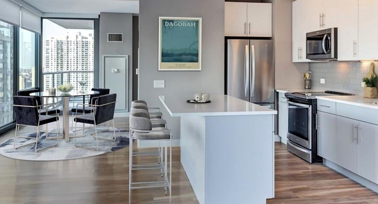Contemporary kitchen with white cabinets, stainless steel appliances, a large island with bar seating, and an adjacent dining area at State and Grand Apartments in Chicago