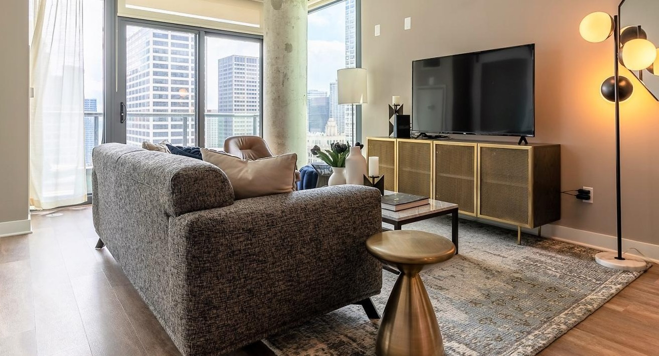 Stylish living room with a comfortable sofa, modern decor, and expansive windows offering picturesque city views at State and Grand Apartments in Chicago