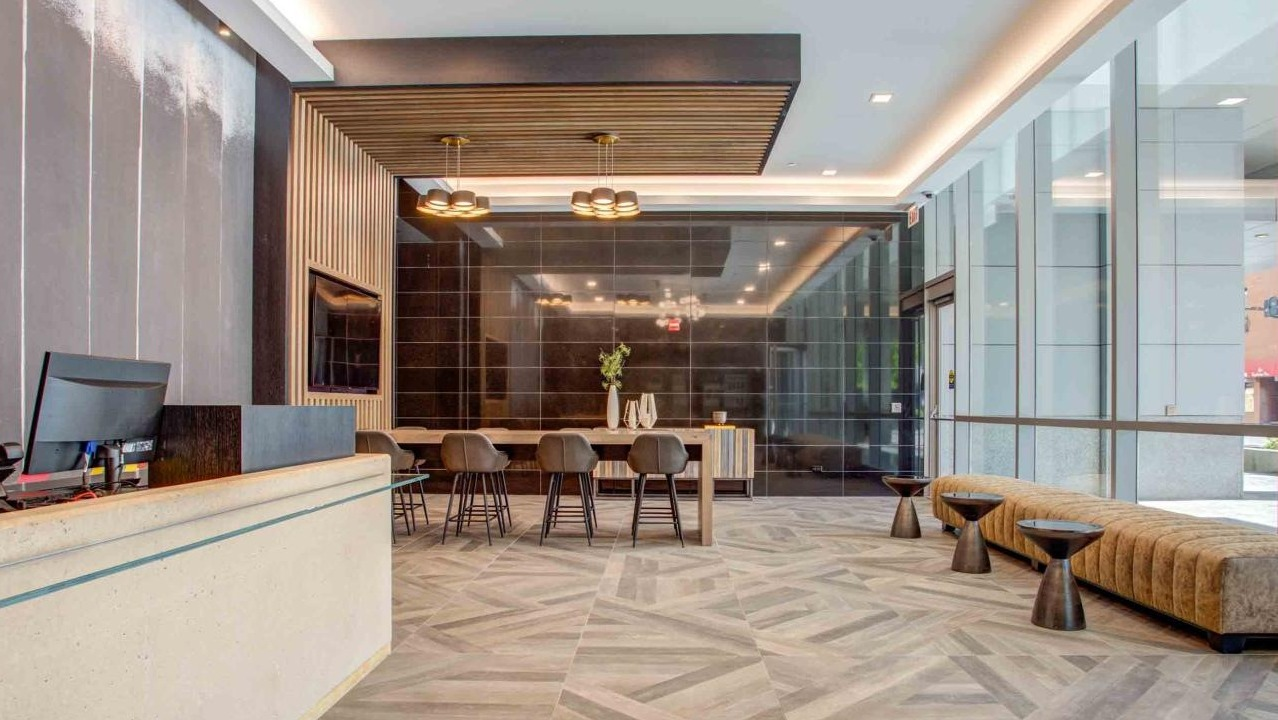 Stylish lobby with a modern reception desk, geometric floor patterns, a communal table, and comfortable lounge seating at State and Grand Apartments in Chicago