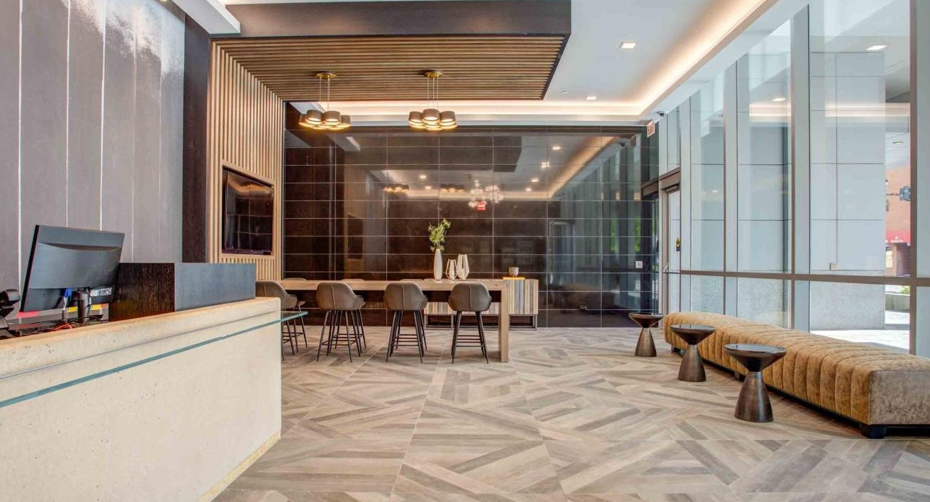 Stylish lobby with a modern reception desk, geometric floor patterns, a communal table, and comfortable lounge seating at State and Grand Apartments in Chicago