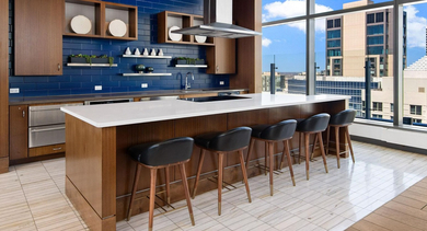 Stylish community kitchen at State & Chestnut in Chicago, featuring a large island with seating, blue subway tile, and stainless steel appliances
