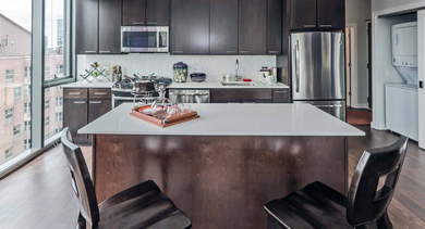 Modern apartment kitchen at State & Chestnut in Chicago, featuring a dark wood island, stainless steel appliances, and an in-unit washer/dryer