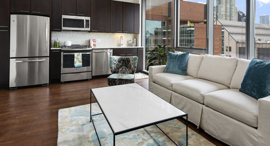 Modern apartment kitchen and living room at State & Chestnut in Chicago, featuring dark wood cabinetry, stainless steel appliances, and a comfortable sofa