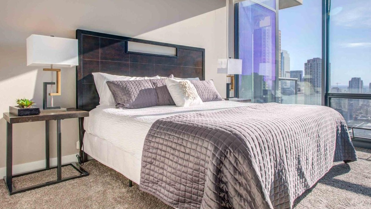 Sophisticated bedroom at State and Grand Apartments in Chicago, featuring a king-size bed, elegant decor, and sweeping cityscape views