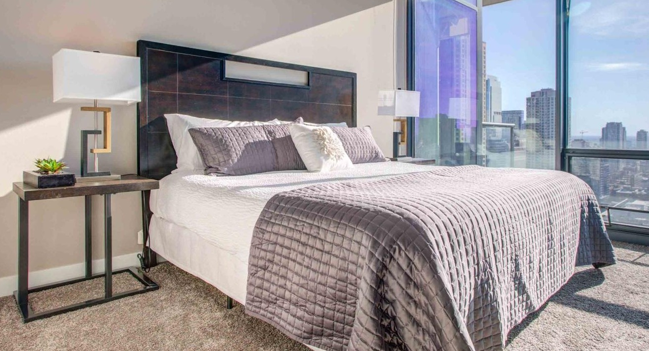 Sophisticated bedroom at State and Grand Apartments in Chicago, featuring a king-size bed, elegant decor, and sweeping cityscape views