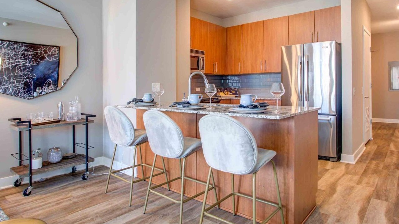 Modern apartment kitchen at State and Grand Apartments in Chicago, featuring a granite island with bar seating, and warm wood cabinetry