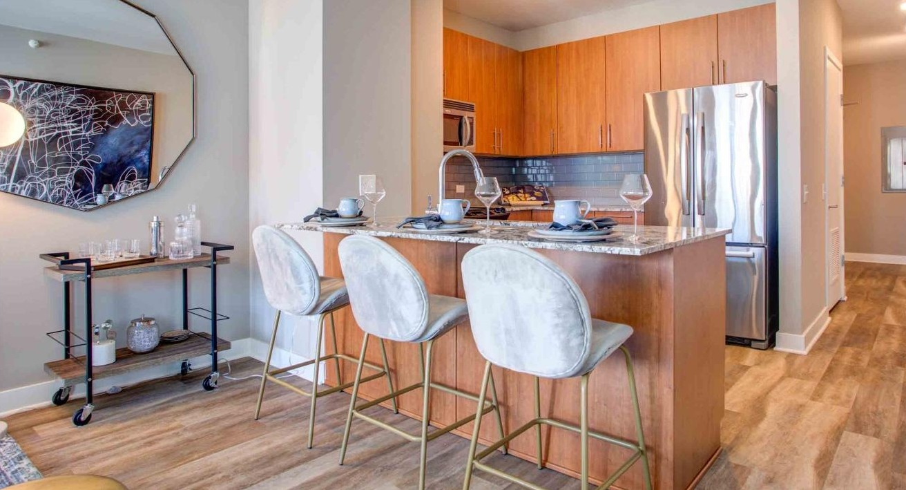 Modern apartment kitchen at State and Grand Apartments in Chicago, featuring a granite island with bar seating, and warm wood cabinetry