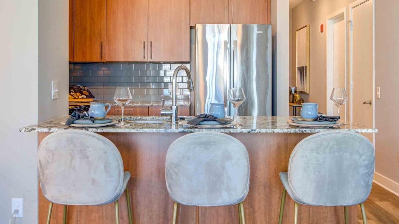 Close-up of the elegant apartment kitchen at State and Grand Apartments in Chicago, featuring a granite island, stylish bar stools, and wood cabinets