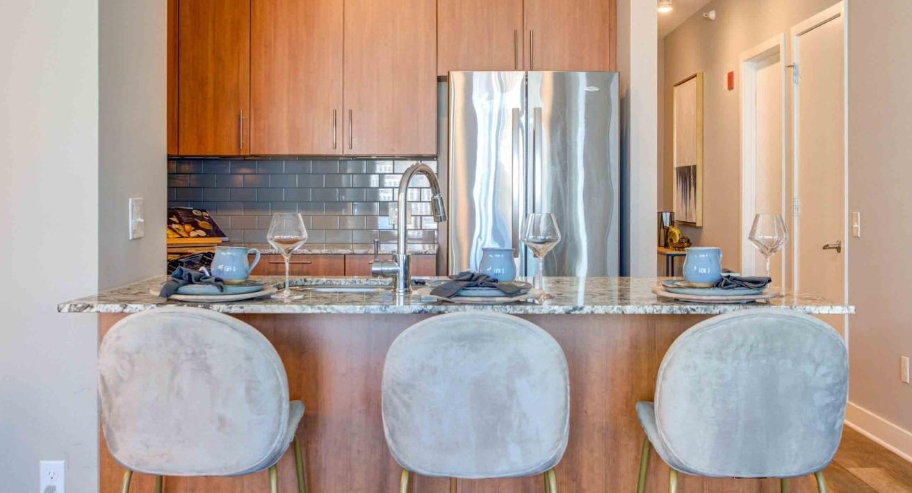 Close-up of the elegant apartment kitchen at State and Grand Apartments in Chicago, featuring a granite island, stylish bar stools, and wood cabinets
