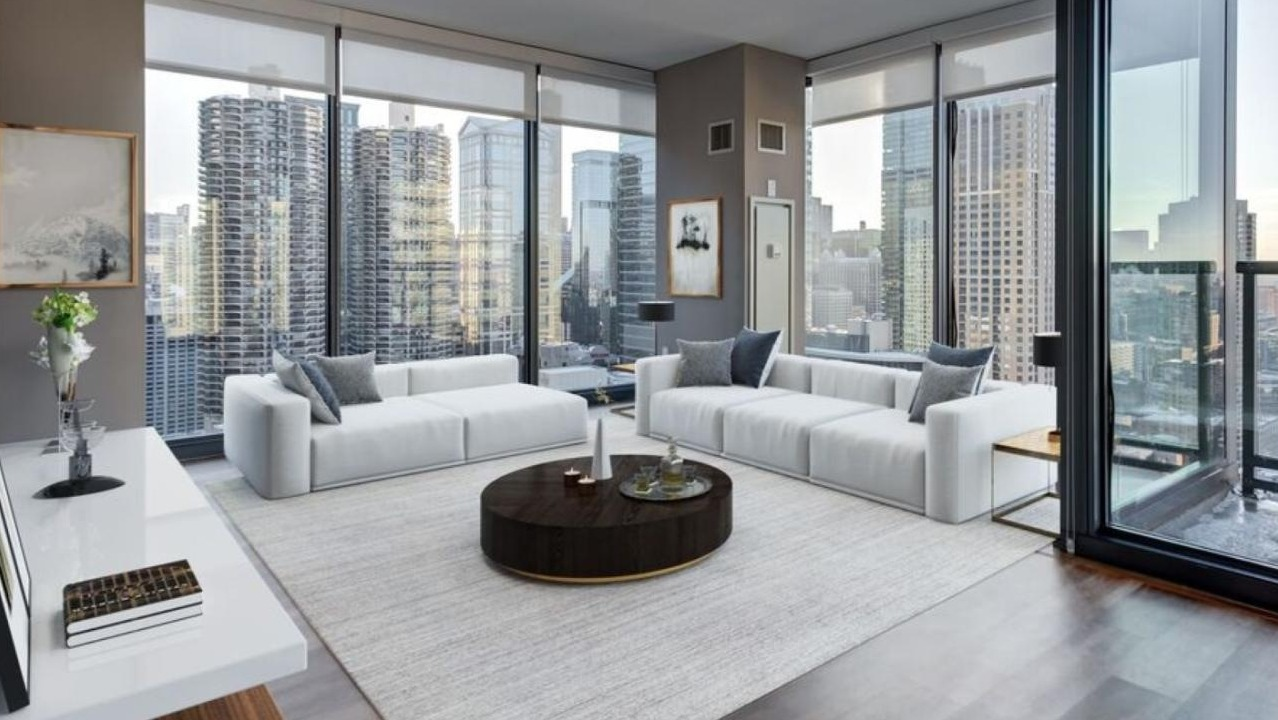 Expansive living room at State and Grand Apartments in Chicago, featuring white sofas, a stylish coffee table, and panoramic city views