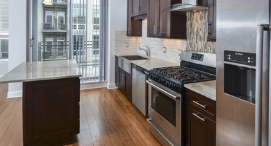 Modern kitchen with dark wood cabinets, stainless steel appliances, and a granite-topped island at The Aberdeen West Loop Luxury Apartments