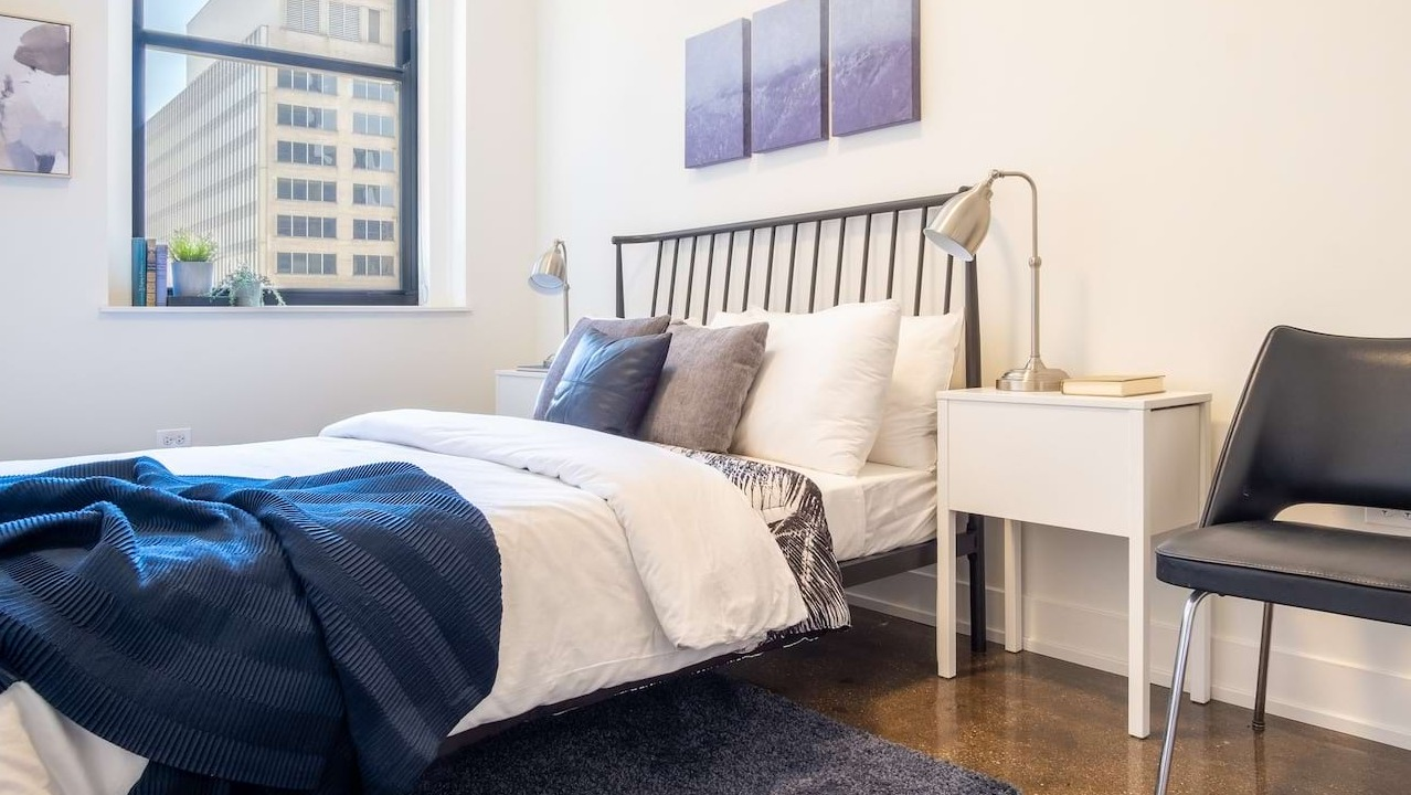 Bright bedroom at The Alfred Apartments in Chicago, with a comfortable bed, modern decor, and a large window offering city views