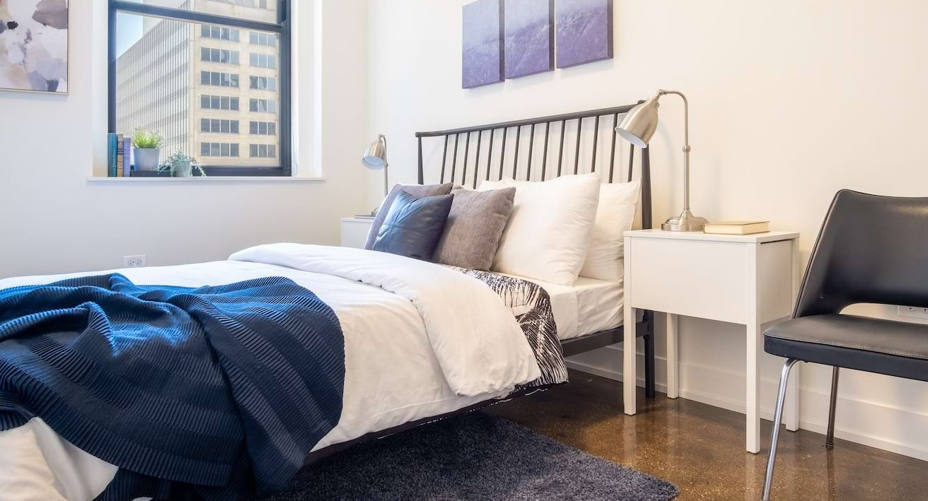 Bright bedroom at The Alfred Apartments in Chicago, with a comfortable bed, modern decor, and a large window offering city views