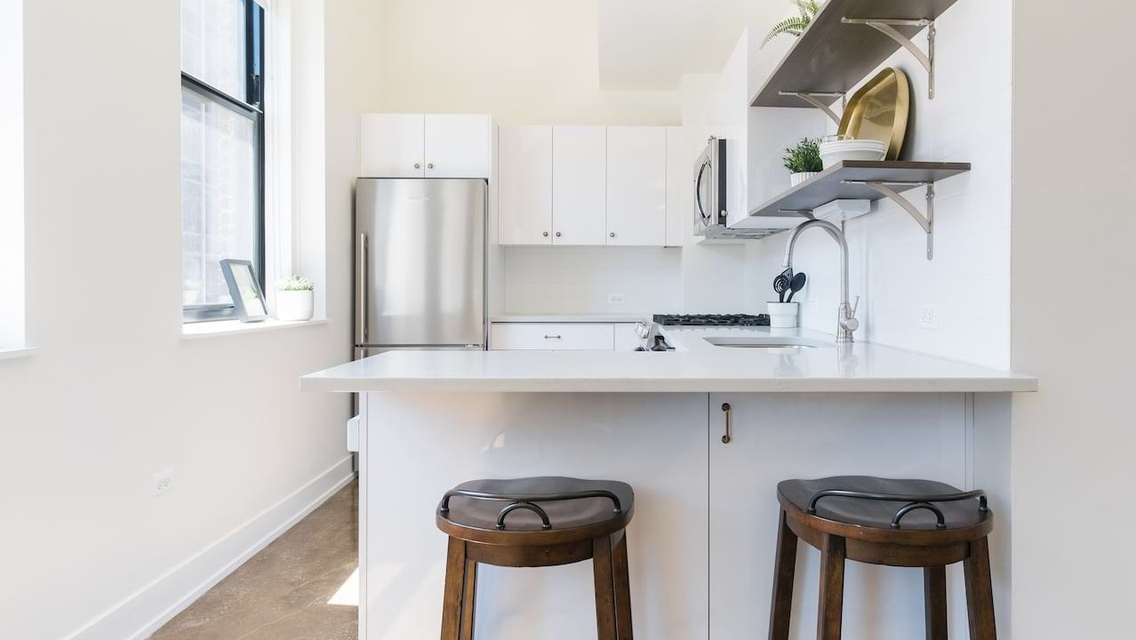 Compact kitchen at The Alfred Apartments in Chicago, with white cabinets, stainless steel appliances, and a small island with seating