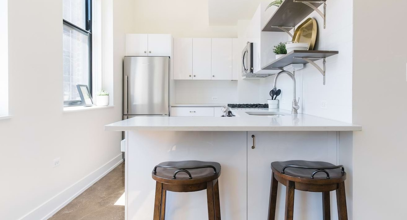 Compact kitchen at The Alfred Apartments in Chicago, with white cabinets, stainless steel appliances, and a small island with seating