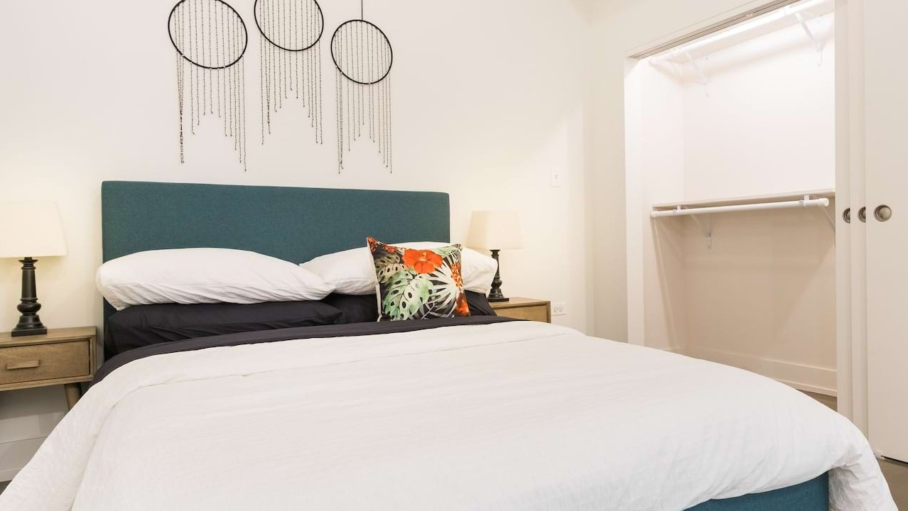 Cozy bedroom at The Alfred Apartments in Chicago, featuring a teal upholstered bed, bedside tables, and an open closet