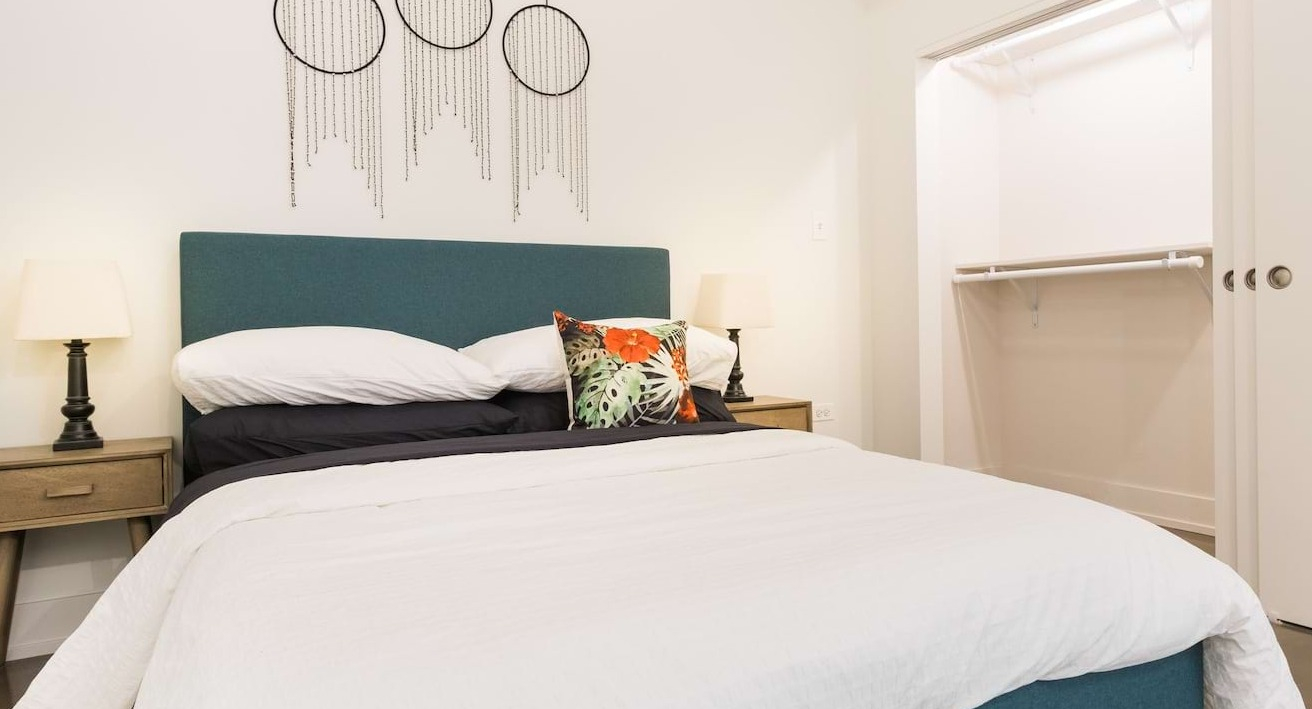 Cozy bedroom at The Alfred Apartments in Chicago, featuring a teal upholstered bed, bedside tables, and an open closet