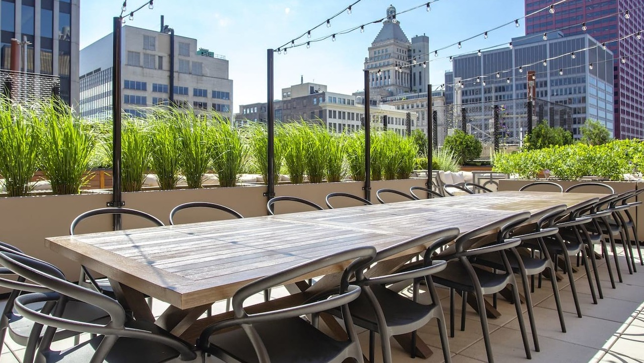 Rooftop dining area at The Alfred Apartments in Chicago, with a long communal table, string lights, and city skyline views