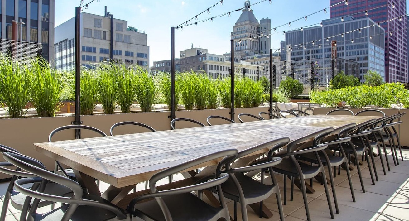 Rooftop dining area at The Alfred Apartments in Chicago, with a long communal table, string lights, and city skyline views