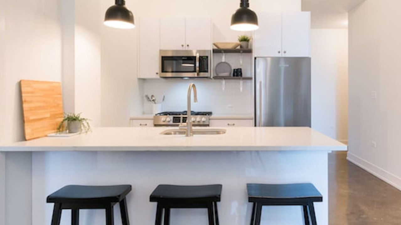 Sleek kitchen at The Alfred Apartments in Chicago, with white cabinets, stainless steel appliances, and a breakfast bar with stools