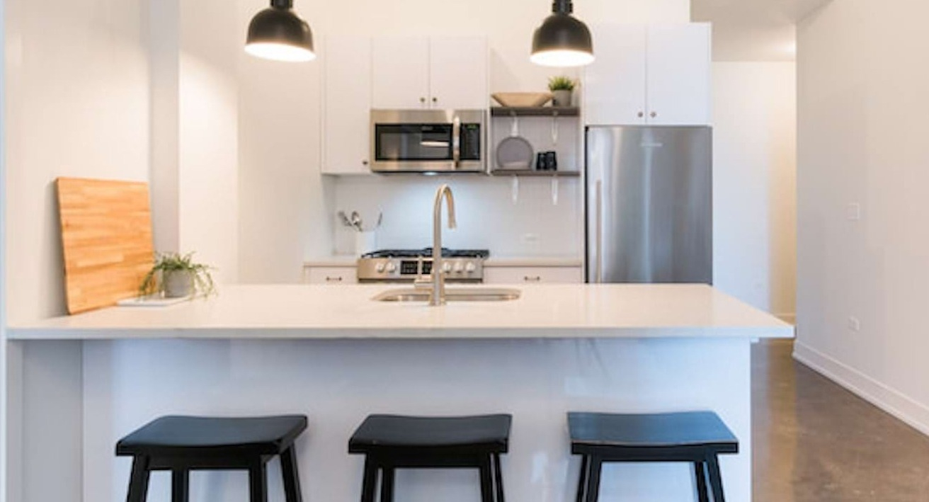 Sleek kitchen at The Alfred Apartments in Chicago, with white cabinets, stainless steel appliances, and a breakfast bar with stools