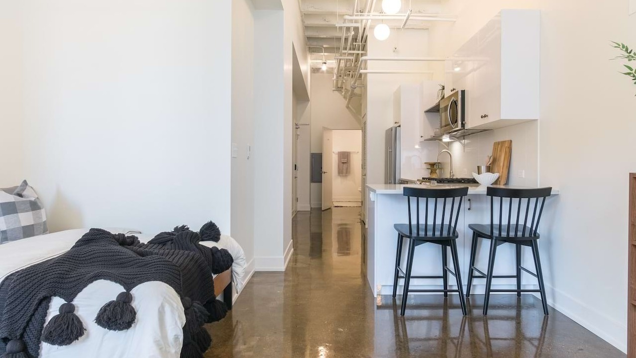 Studio apartment at The Alfred Apartments in Chicago, showcasing a compact kitchen with a breakfast bar and cozy bed