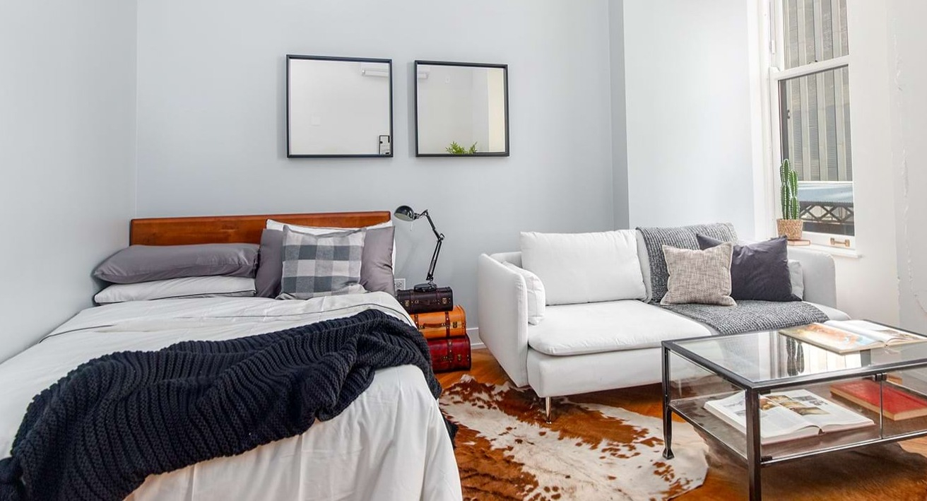 Studio apartment at The Alfred Apartments in Chicago, combining a comfortable bed, sofa, and living area with a large window