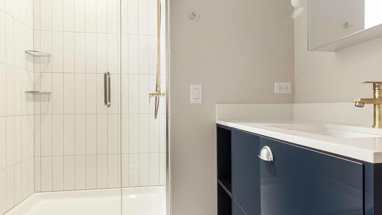 Modern apartment bathroom at The Ardus in Chicago, featuring a sleek vanity and a spacious walk-in shower with white tiled walls