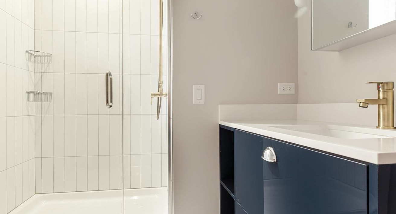 Modern apartment bathroom at The Ardus in Chicago, featuring a sleek vanity and a spacious walk-in shower with white tiled walls