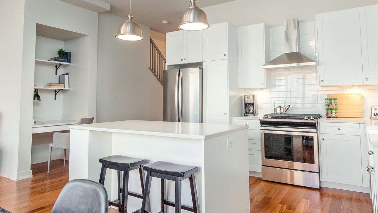 Modern apartment kitchen and discreet home office nook at The Ardus in Chicago, featuring white cabinets, an island, and pendant lighting