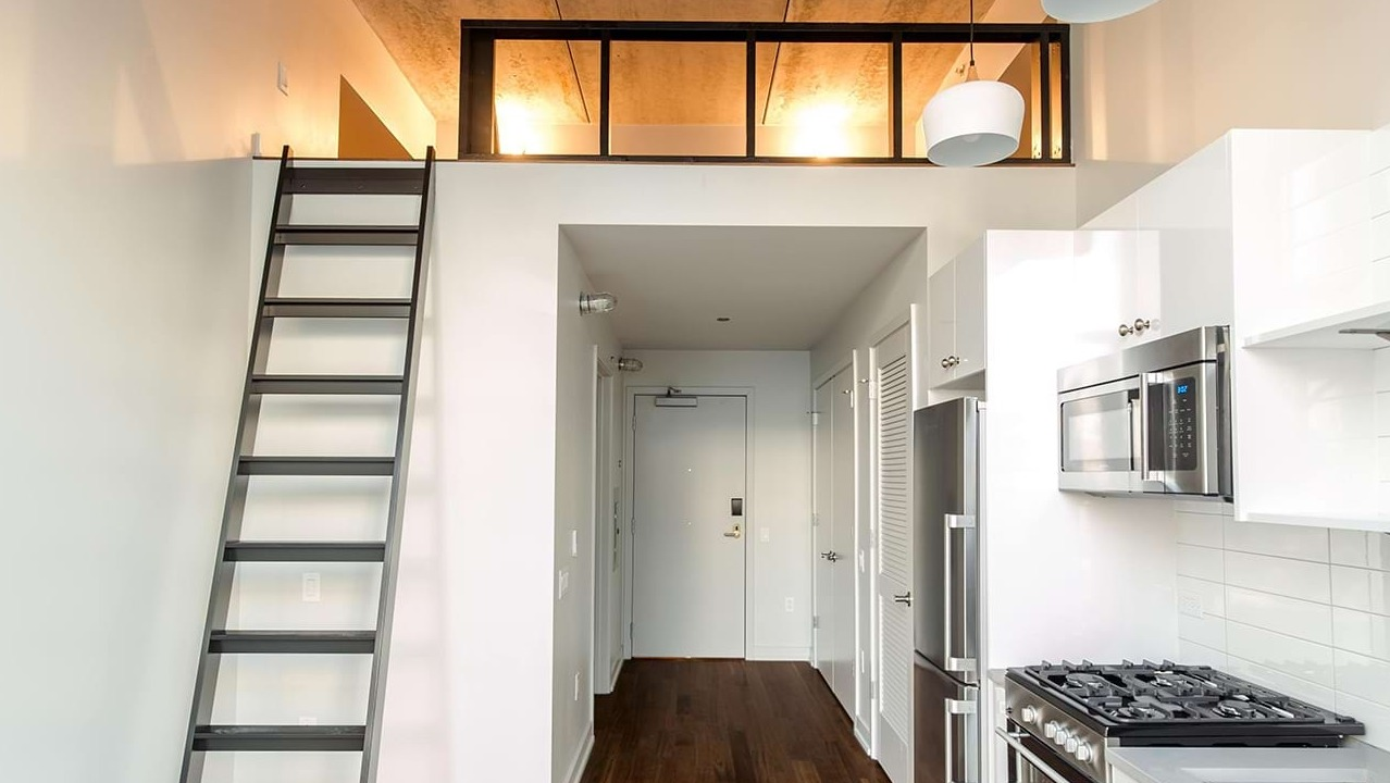 Stylish loft apartment kitchen at The Ardus in Chicago, featuring white cabinetry, stainless steel appliances, and a ladder leading to a loft space
