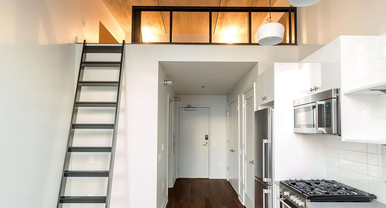 Stylish loft apartment kitchen at The Ardus in Chicago, featuring white cabinetry, stainless steel appliances, and a ladder leading to a loft space