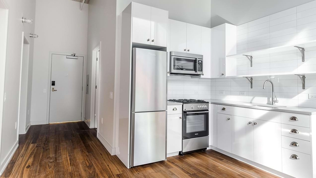 Bright and modern apartment kitchen at The Ardus in Chicago, featuring white cabinetry, stainless steel appliances, and wood flooring