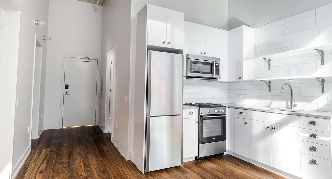 Bright and modern apartment kitchen at The Ardus in Chicago, featuring white cabinetry, stainless steel appliances, and wood flooring