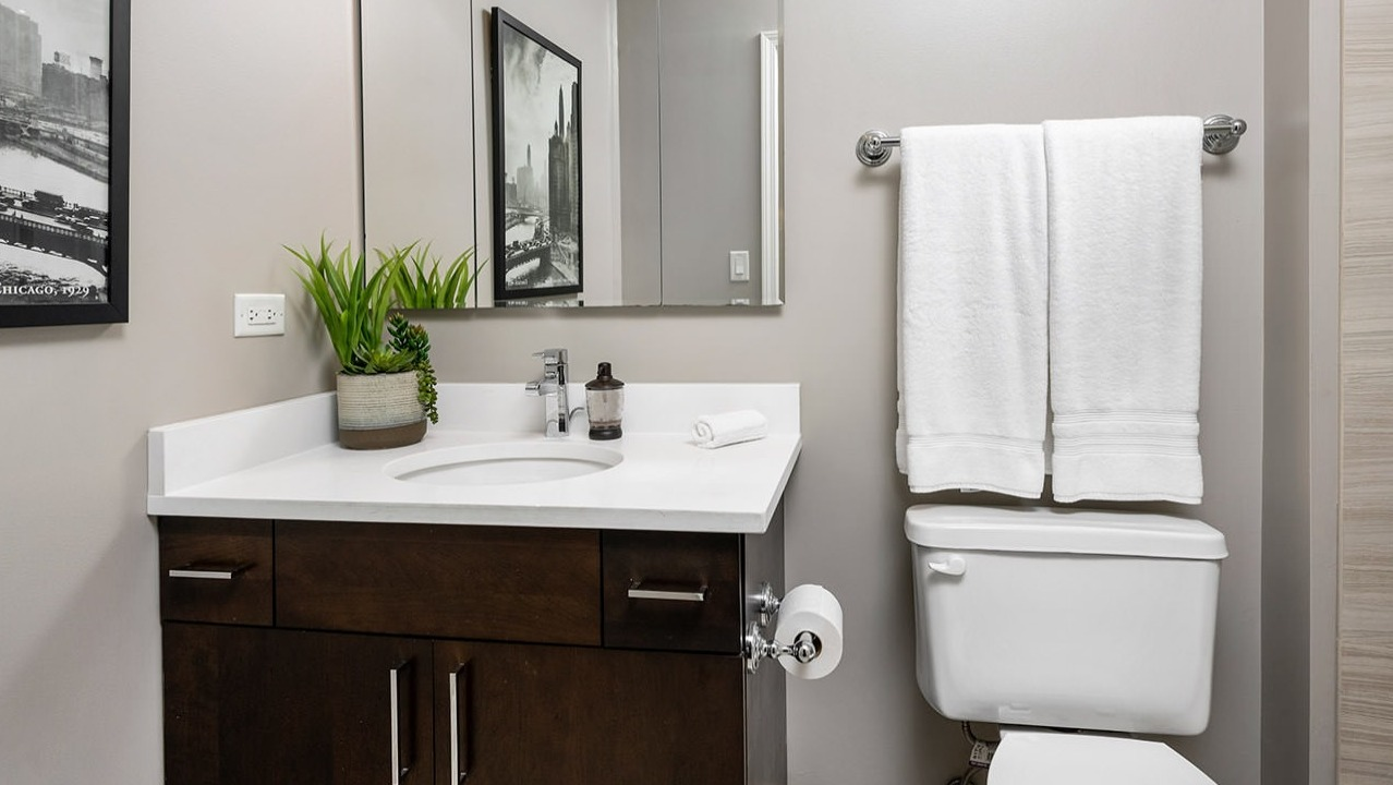 Contemporary bathroom with a dark wood vanity, white countertop, large mirror, and clean tiled shower at The Bernardin Apartments in Chicago