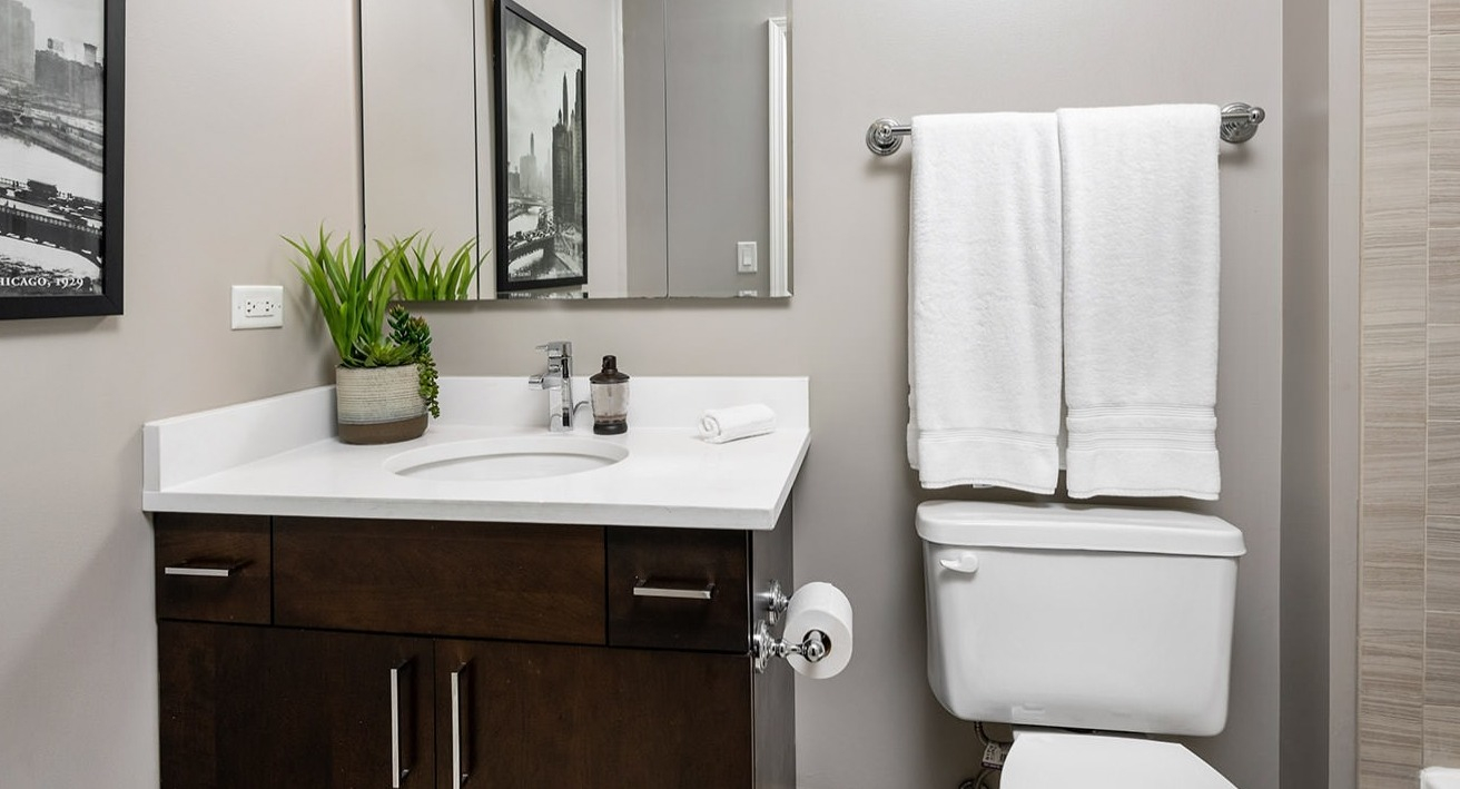 Contemporary bathroom with a dark wood vanity, white countertop, large mirror, and clean tiled shower at The Bernardin Apartments in Chicago