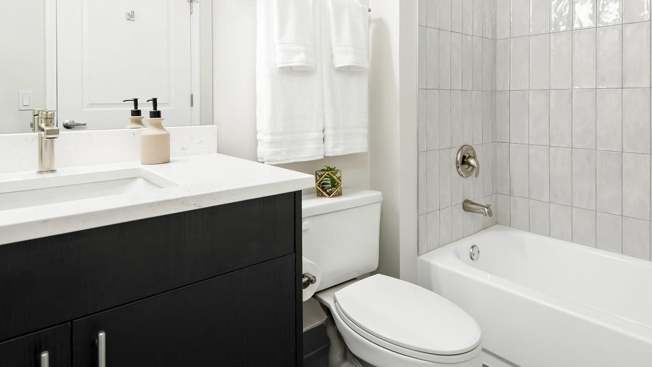 Clean and modern bathroom with a dark vanity, white countertop, and a tiled shower-over-tub combination at The Bernardin Apartments in Chicago