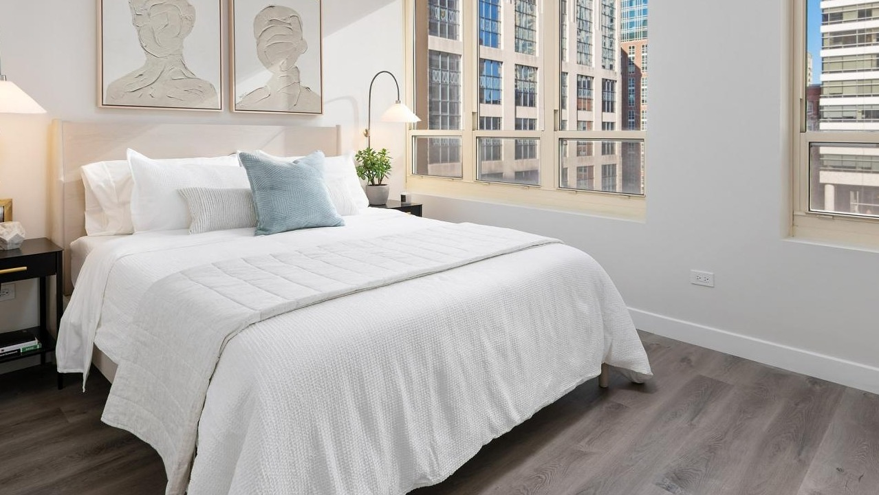 Serene bedroom with a queen-sized bed, soft lighting, and large windows offering natural light and city views at The Bernardin Apartments in Chicago