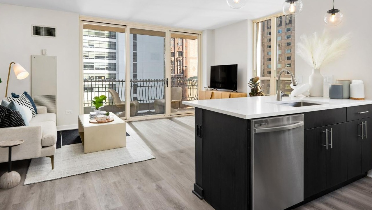 Bright open-concept living room and kitchen with a modern island, elegant decor, and a private balcony at The Bernardin Apartments in Chicago